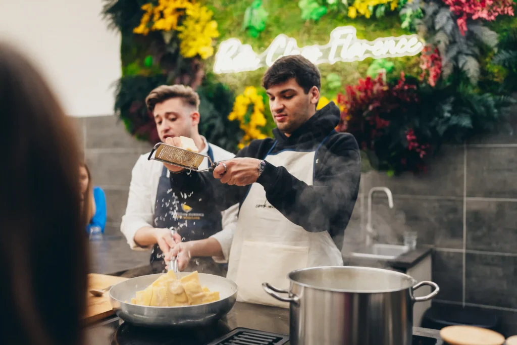 person putting some parmigian cheese on the pasta while a chef is cooking